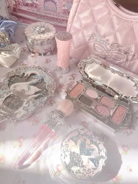 Coquette makeup collection featuring pink quilted bag, silver palettes, and brushes on a floral tablecloth
